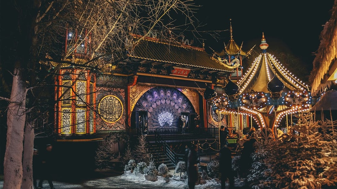 Tivoli Gardens at night with illuminated carousel and ornate building in Copenhagen.