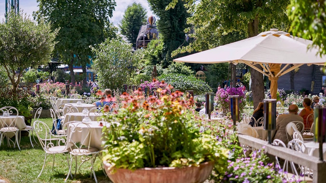 Outdoor dining area with tables and chairs surrounded by flowers at Tivoli Gardens.