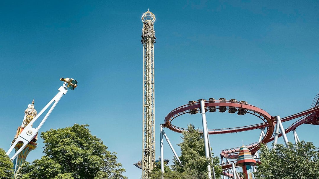 Roller coasters and rides at Tivoli Gardens, Copenhagen, under a clear blue sky.