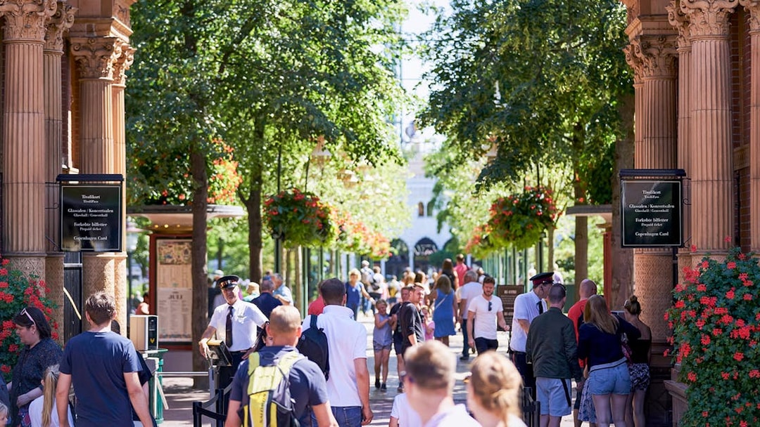 Visitors entering Tivoli Gardens in Copenhagen under ornate arches with lush greenery.