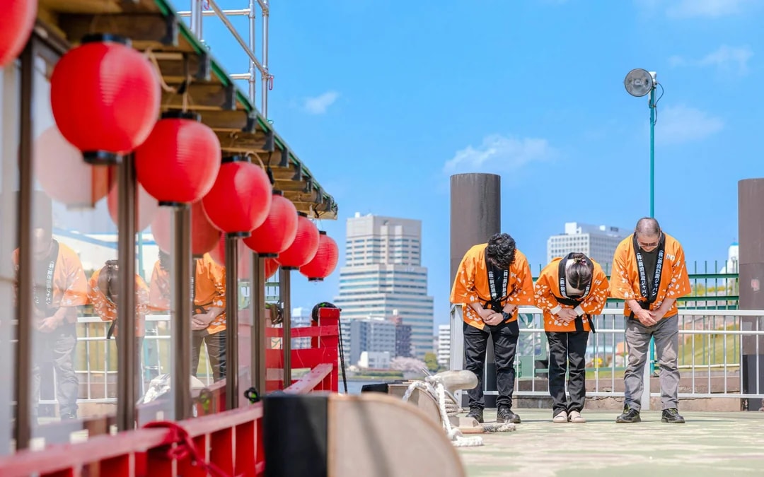 Crew members in traditional attire bowing on the deck of a Yakatabune in Japan.