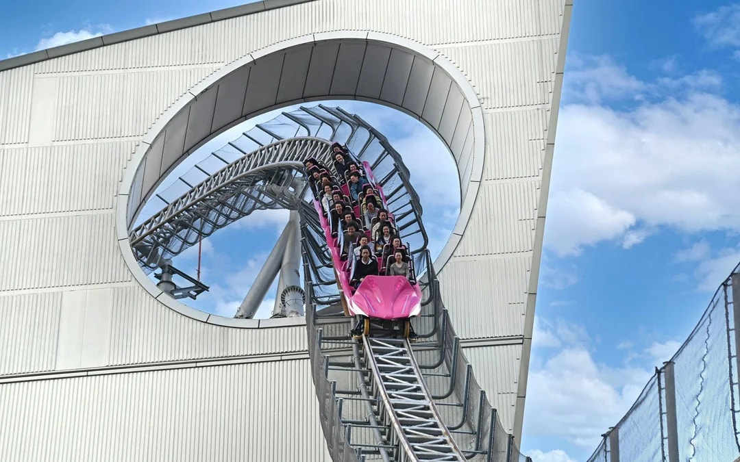 Roller coaster descending through a building loop near Tokyo Dome.