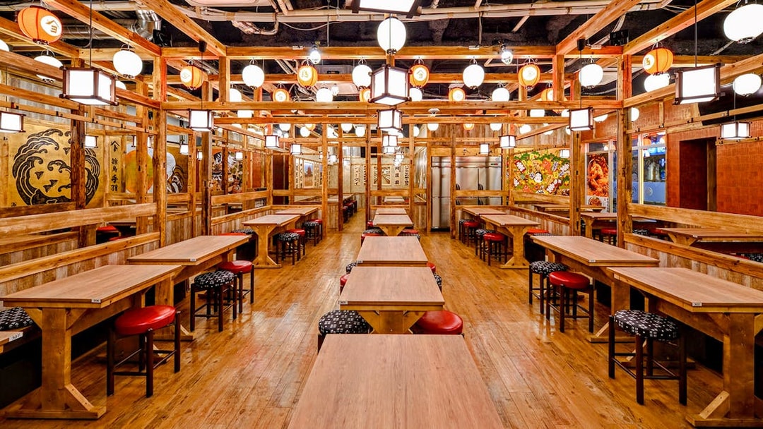 Interior of a Japanese Izakaya with wooden tables, red stools, and traditional lanterns.