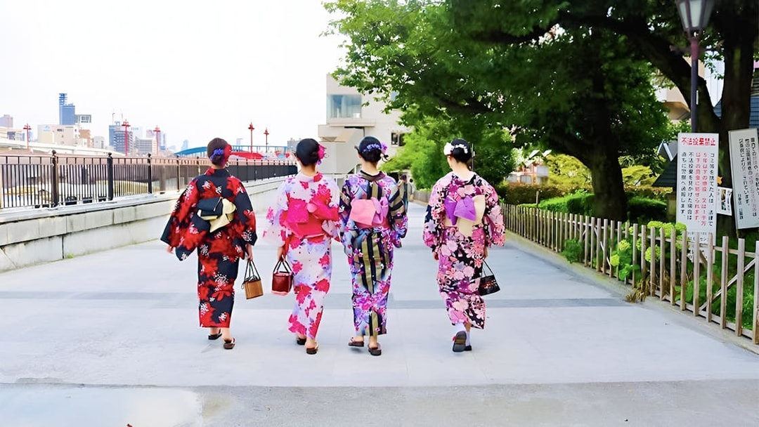 Women in colorful kimonos walking in Asakusa, Tokyo, near a riverside path.
