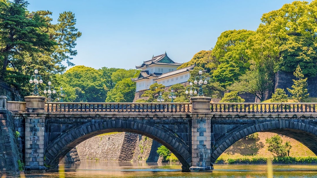 Tokyo Imperial Palace with Nijubashi Bridge in foreground, surrounded by lush greenery.