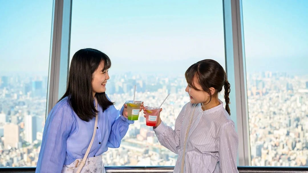 Tourists toasting with drinks on Tembo Deck overlooking cityscape.