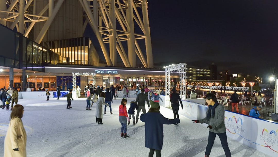 People ice skating at night near Tokyo Skytree, illuminated with festive lights.
