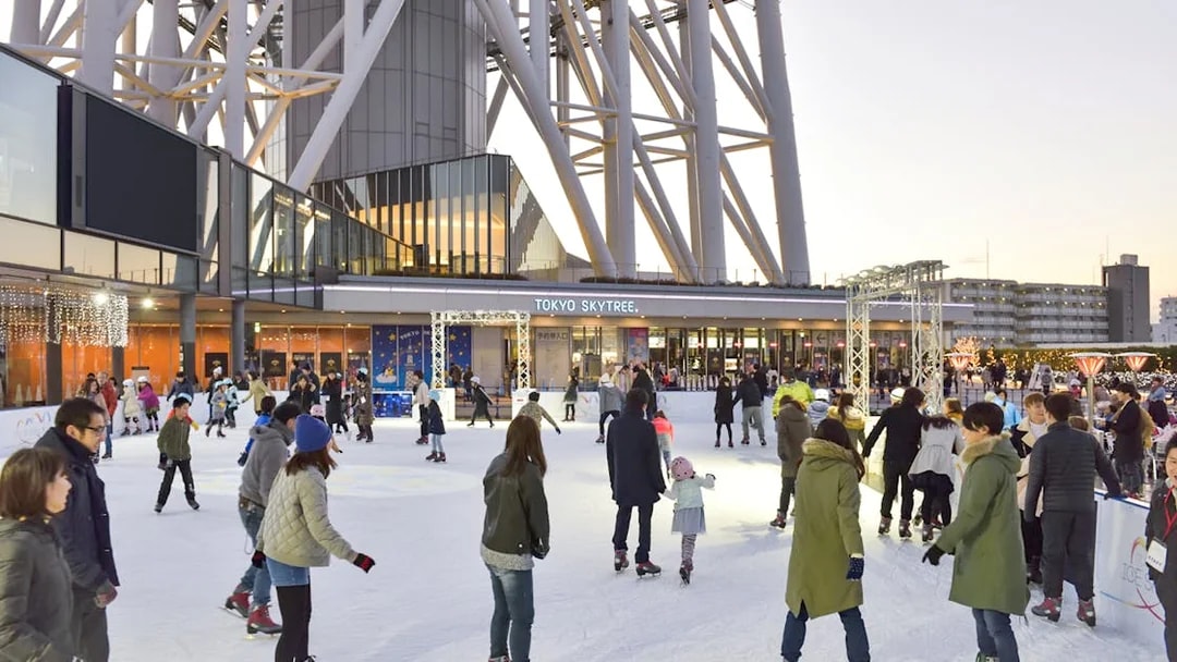 People ice skating at the base of Tokyo Skytree in the evening.