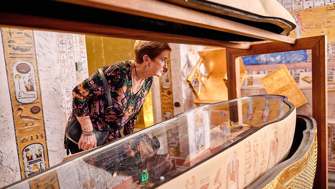 Visitor examines open sarcophagus with hieroglyphs at Tomb of the Pharaoh exhibit.