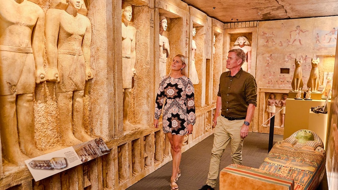 Visitors exploring the Tomb of the Pharaohs exhibit with ancient Egyptian statues and sarcophagus.