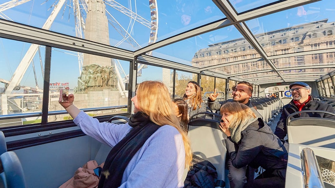 Tourists enjoying Brussels Discovery Hop on Hop off bus tour with Ferris wheel view.