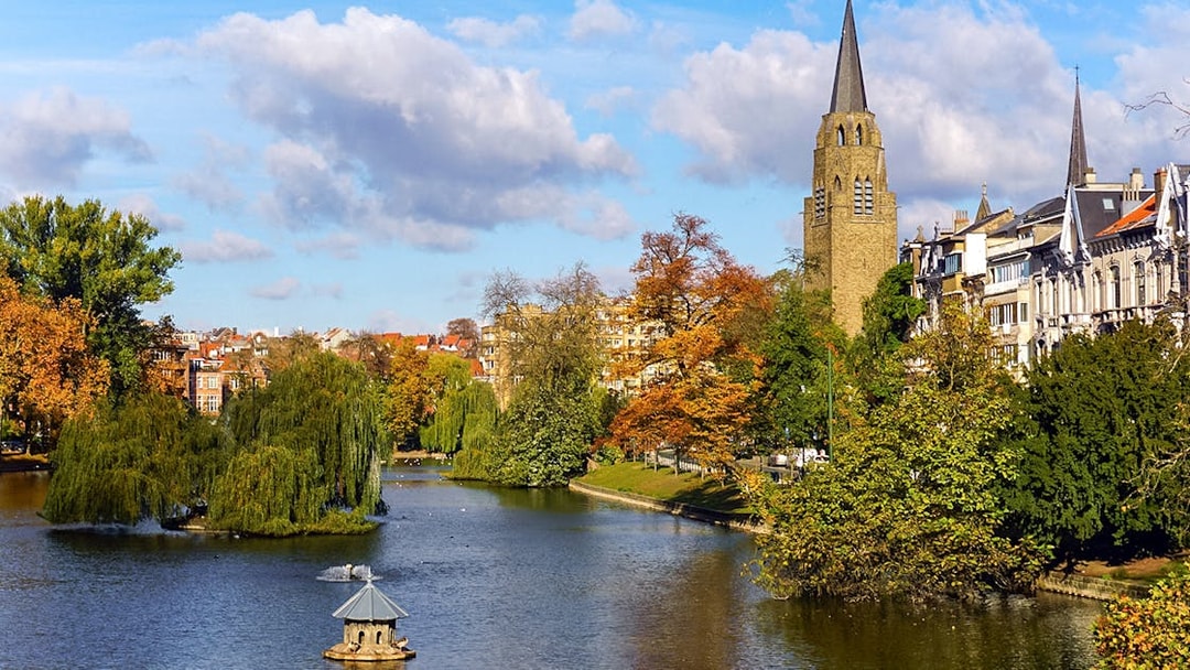 Brussels Ixelles Pond with church tower and autumn trees in Flagey Park.