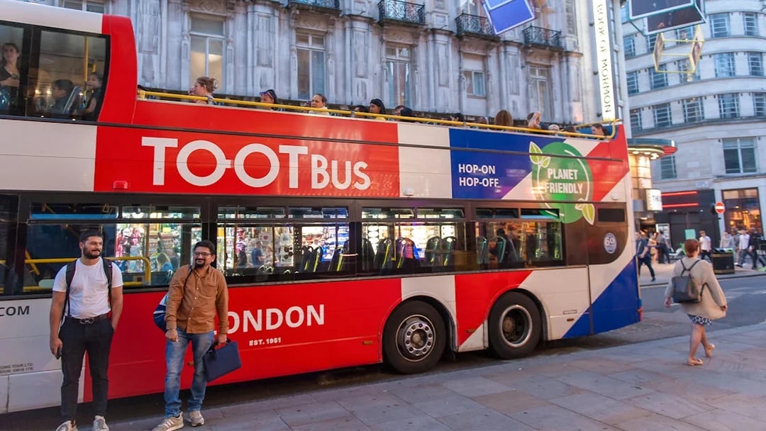 Open-top tour bus in London at night with people sightseeing.
