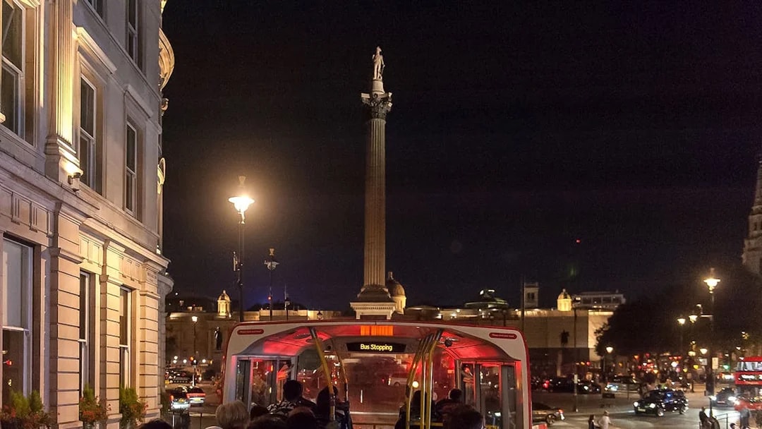 Open-top bus tour at night near Nelson's Column, London.