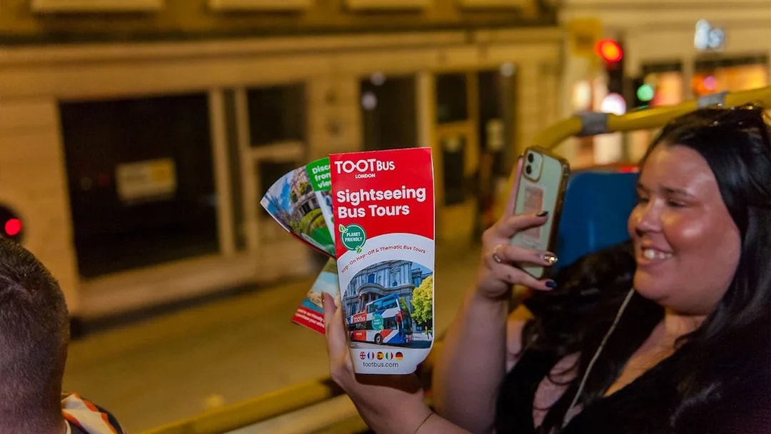 Sightseeing bus tour brochure held by a person on a night tour in London.