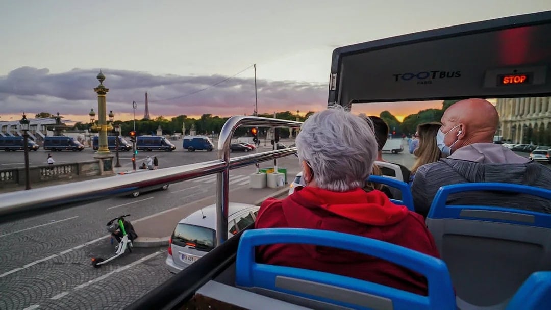 Open-top bus tour in Paris with view of Eiffel Tower at sunset.