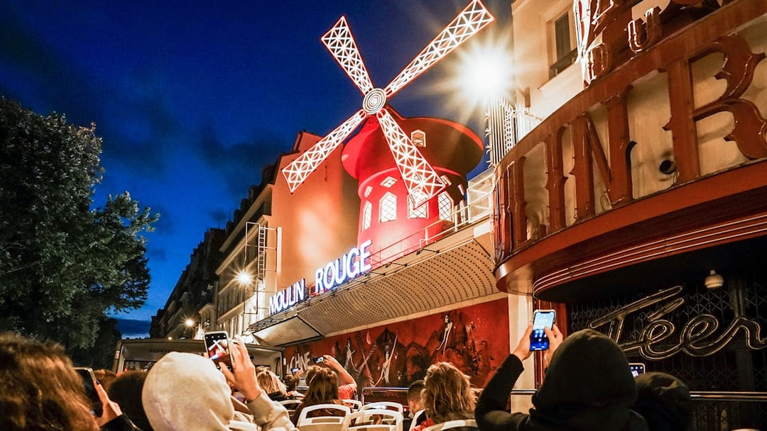 Tourists on Tootbus viewing the illuminated Moulin Rouge in Paris at night.