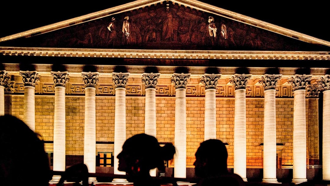 Illuminated facade of La Madeleine in Paris at night with silhouetted figures in foreground.