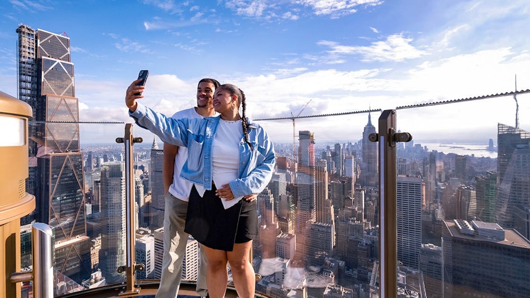 Couple taking a selfie at Top of the Rock Observation Deck with New York City skyline.