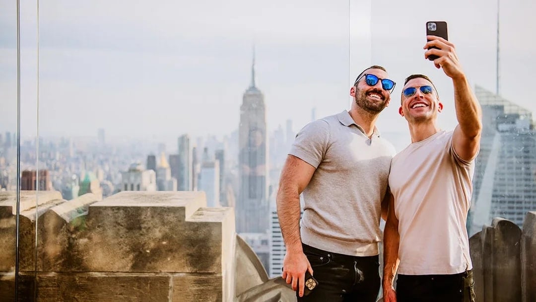 Two men taking a selfie with New York City skyline and Empire State Building from Top of the Rock.
