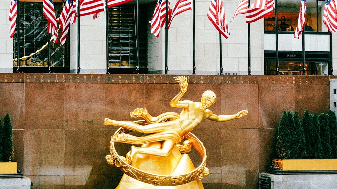 Prometheus Statue at Rockefeller Center with American flags in the background.