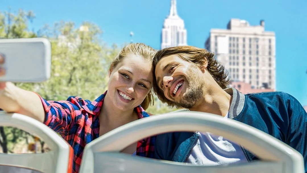 Couple taking selfie on New York Hop On Hop Off bus with Empire State Building.