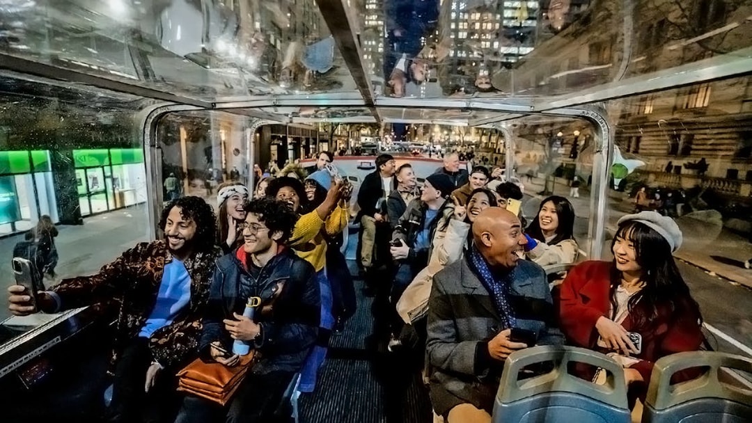 Tourists enjoying a night city view from an open-top bus on a hop-on hop-off tour.
