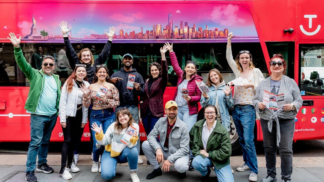 Group of tourists with Hop-On Hop-Off Pass in front of a red tour bus in New York City.