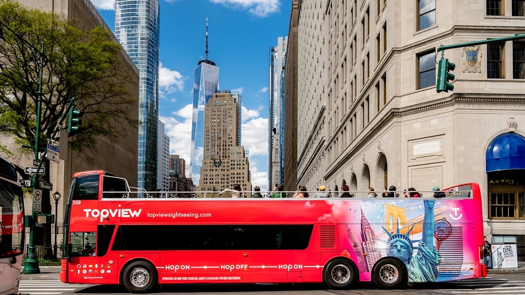 Red double-decker tour bus in New York City with One World Trade Center in background.