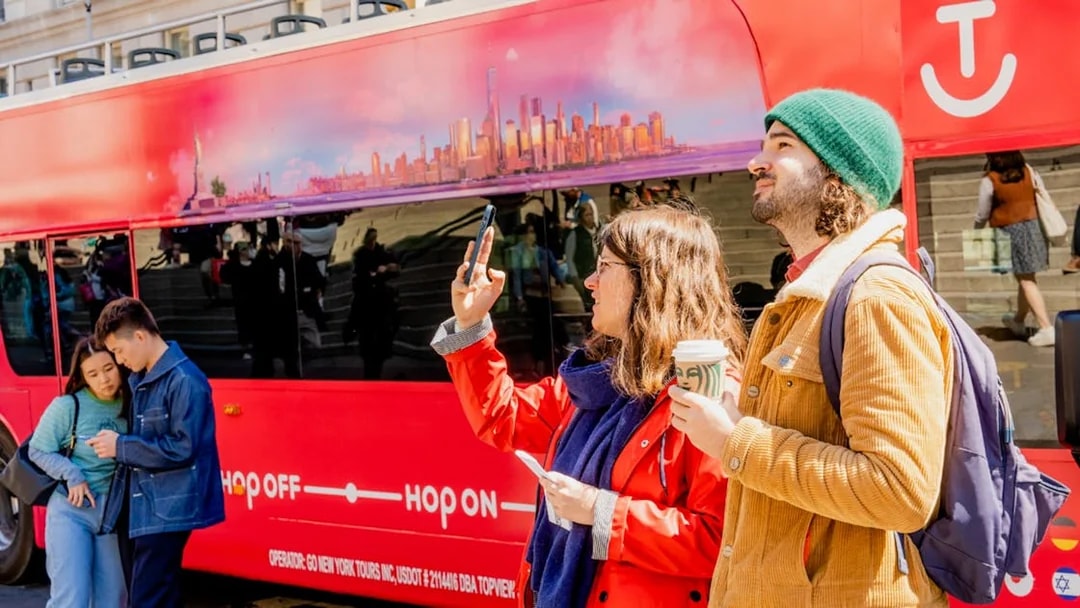 Hop-On Hop-Off bus with tourists taking photos in a city setting.