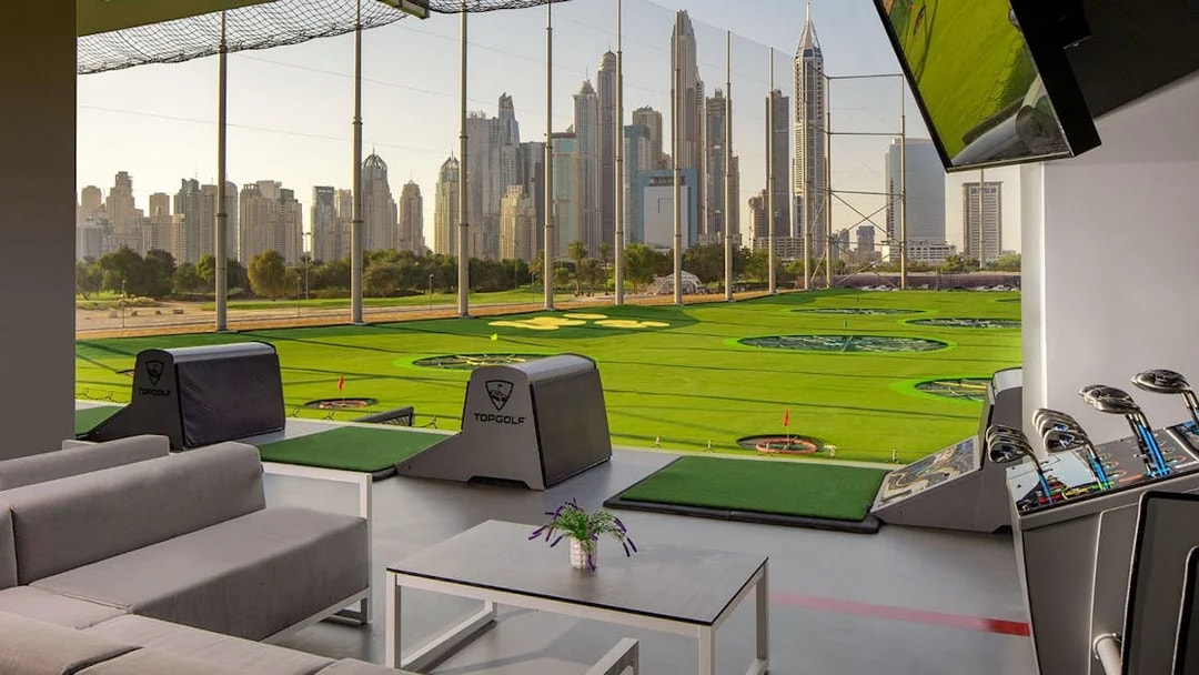 Topgolf Dubai bay with city skyline view and golf equipment.