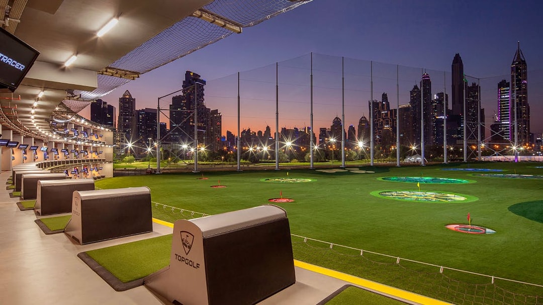 Topgolf Dubai driving range with city skyline at sunset.