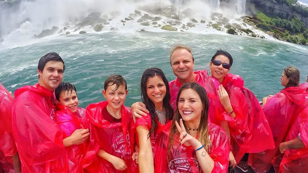 Tourists in red ponchos on a Niagara Falls cruise with waterfalls in the background.