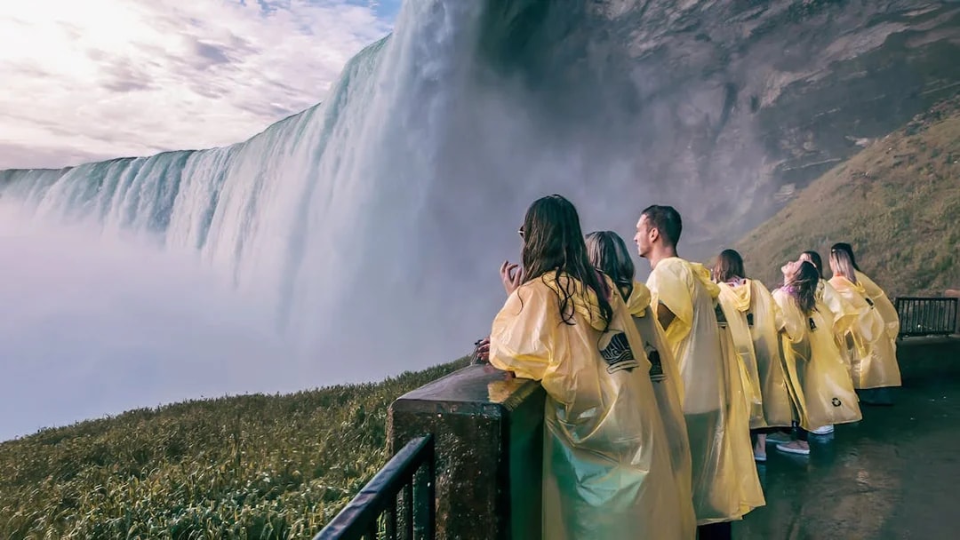 Visitors in yellow ponchos view Niagara Falls from a platform on a day tour from Toronto.