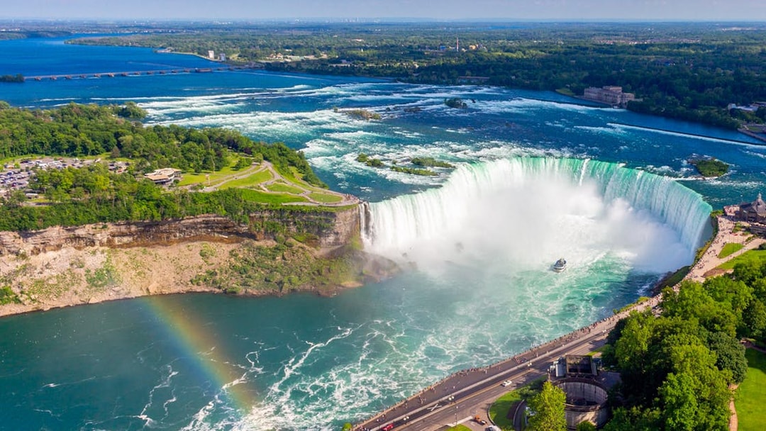 Aerial view of Niagara Falls with a rainbow and tour boat below.