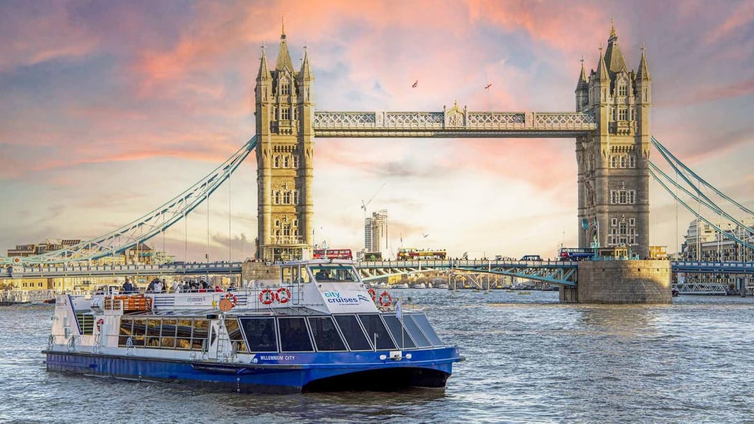 Dinner cruise boat on the Thames River passing by Tower Bridge at sunset.