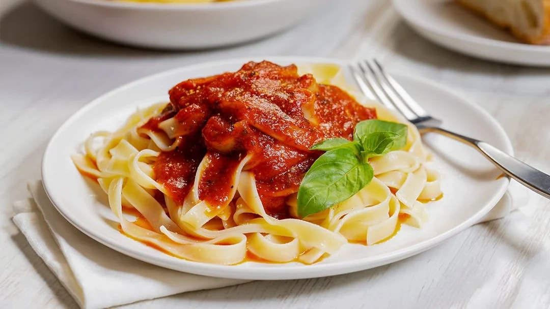 Fettuccine pasta with tomato sauce and basil on a white plate.