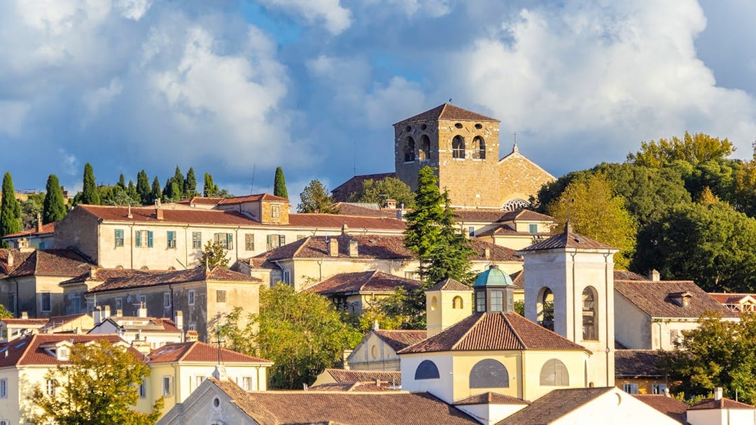 Historic buildings on San Giusto Hill, Trieste, with a church tower and lush greenery.