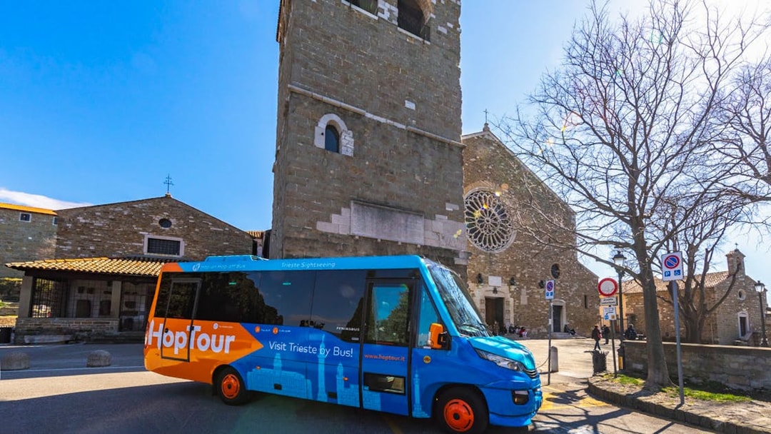Hop-on hop-off bus in front of historic church in Trieste, Italy.