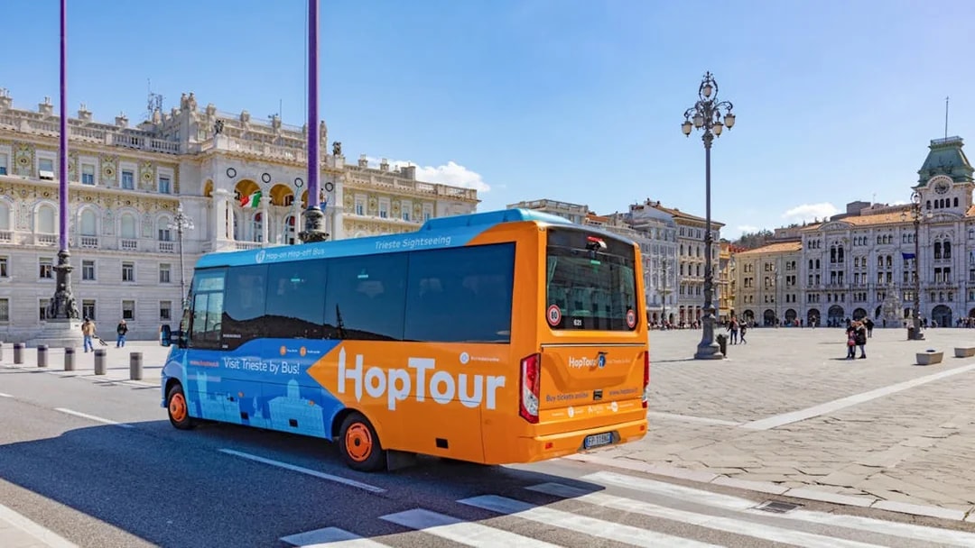 Trieste hop-on hop-off bus near Piazza Unità d'Italia with city landmarks.