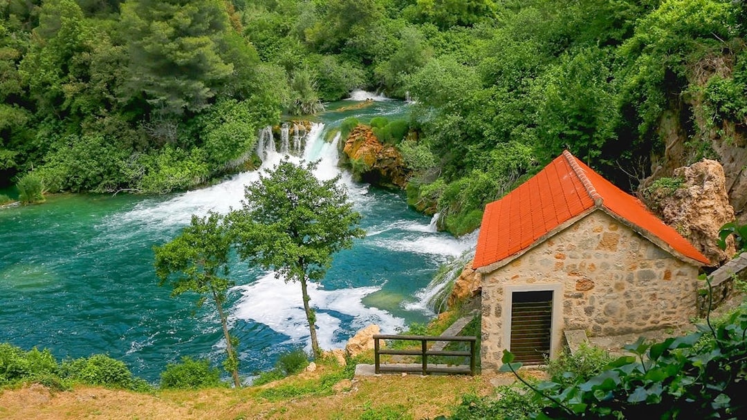 Waterfall and stone house at Krka National Park, Croatia, surrounded by lush greenery.