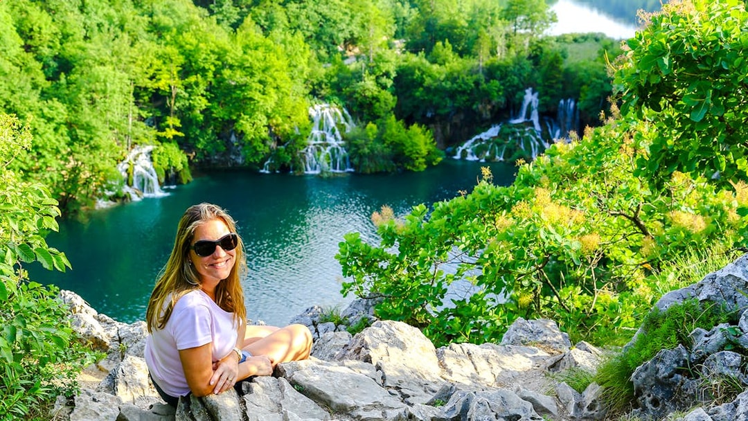 Tourist sitting on a rock overlooking waterfalls at Plitvice Lakes, Croatia.