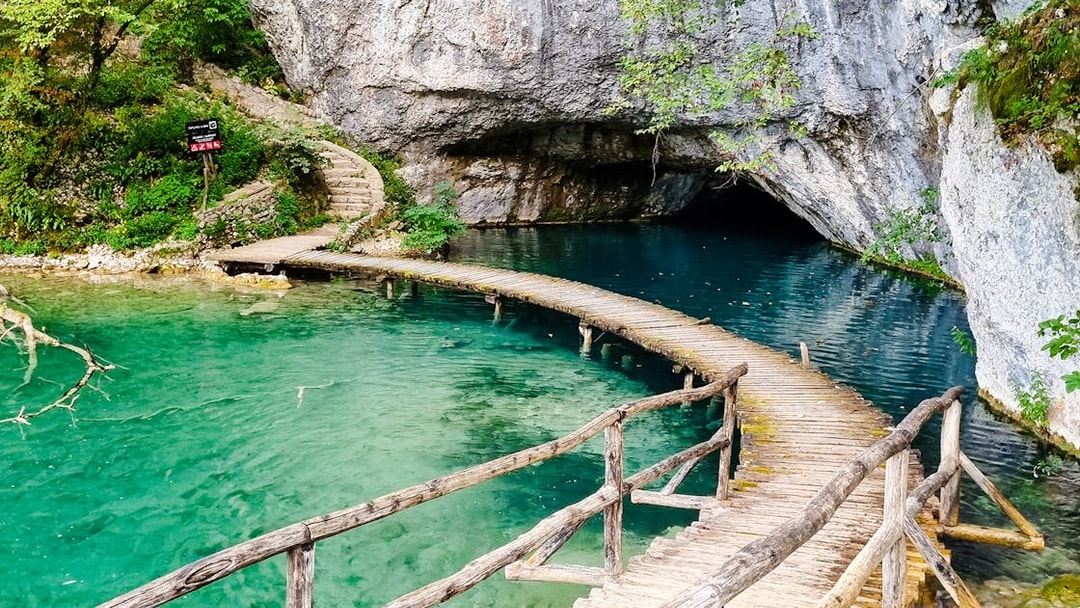 Curved wooden bridge over turquoise lake at Plitvice Lakes National Park.