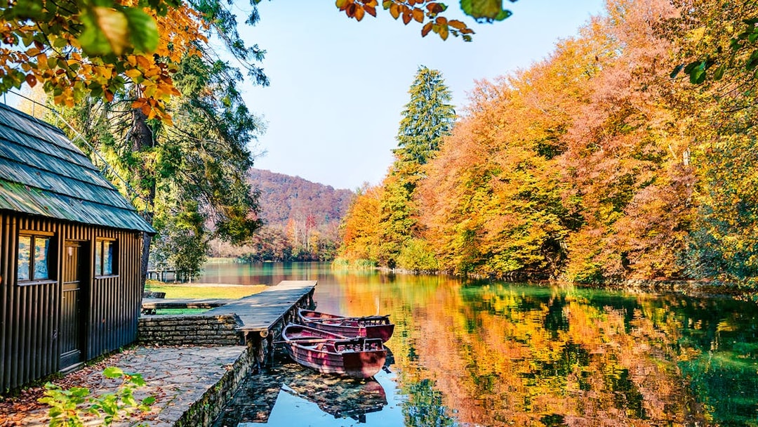 Boats docked on a clear lake surrounded by autumn trees in Plitvice National Park.