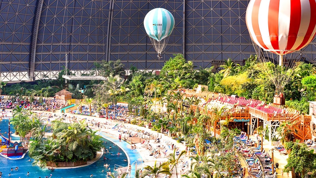 Tropical Islands Resort indoor beach with palm trees and hot air balloons.