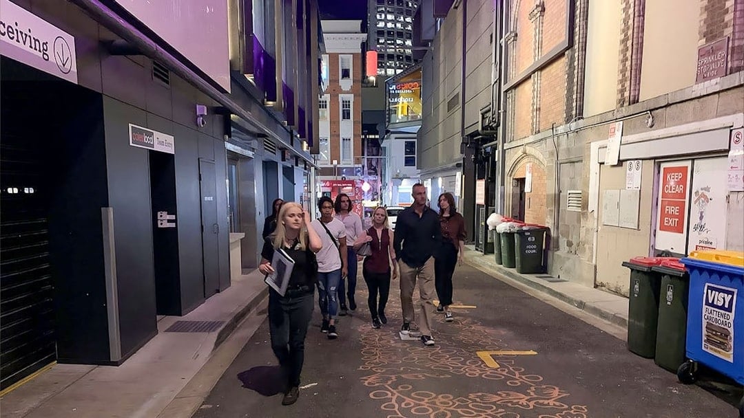 Group walking through a dimly lit alley in Brisbane on a true crime tour.