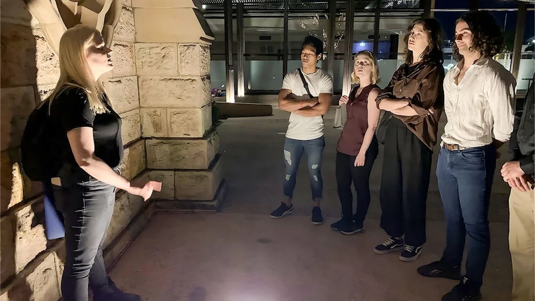 Tour guide narrating Brisbane's true crime stories to a group at night.