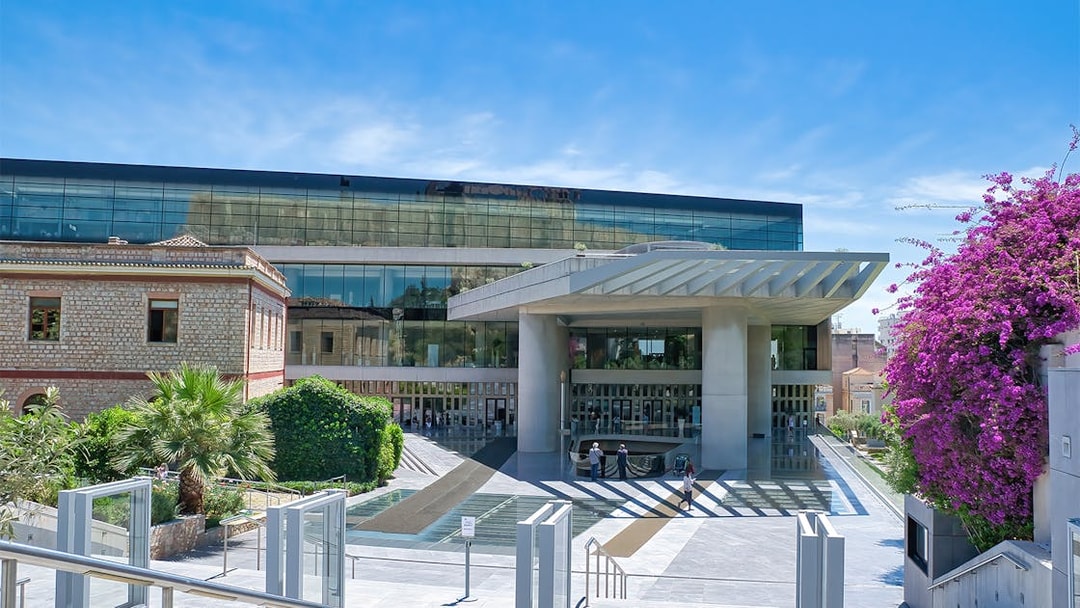 Acropolis Museum entrance in Athens, Greece, with modern architecture and vibrant bougainvillea.