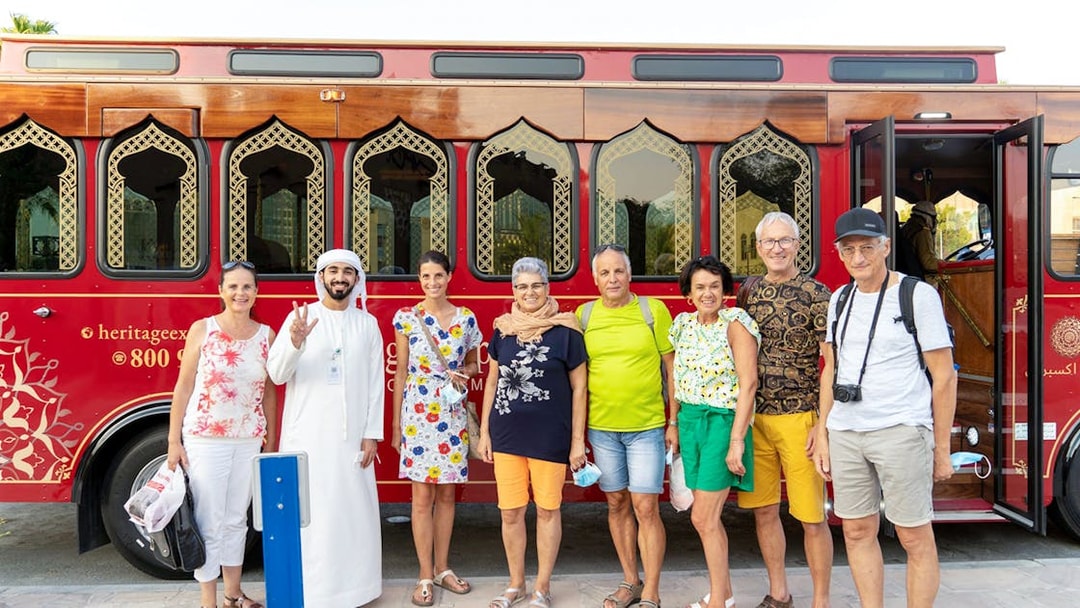 Tourists with a guide in front of a traditional red Dubai tour bus.