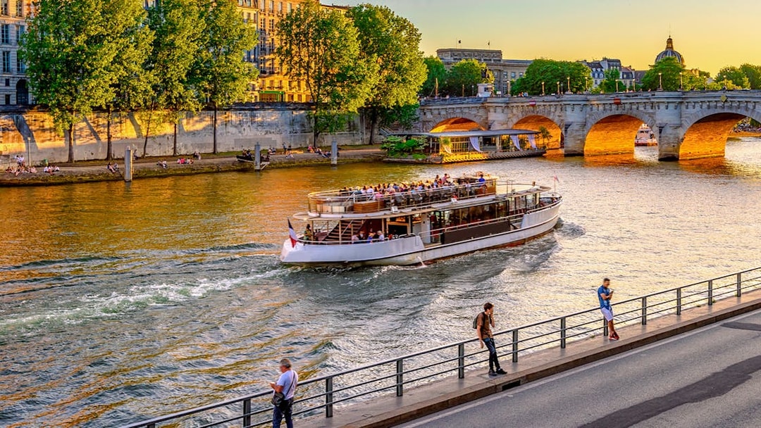 Seine River cruise boat passing under a bridge in Paris, France at sunset.